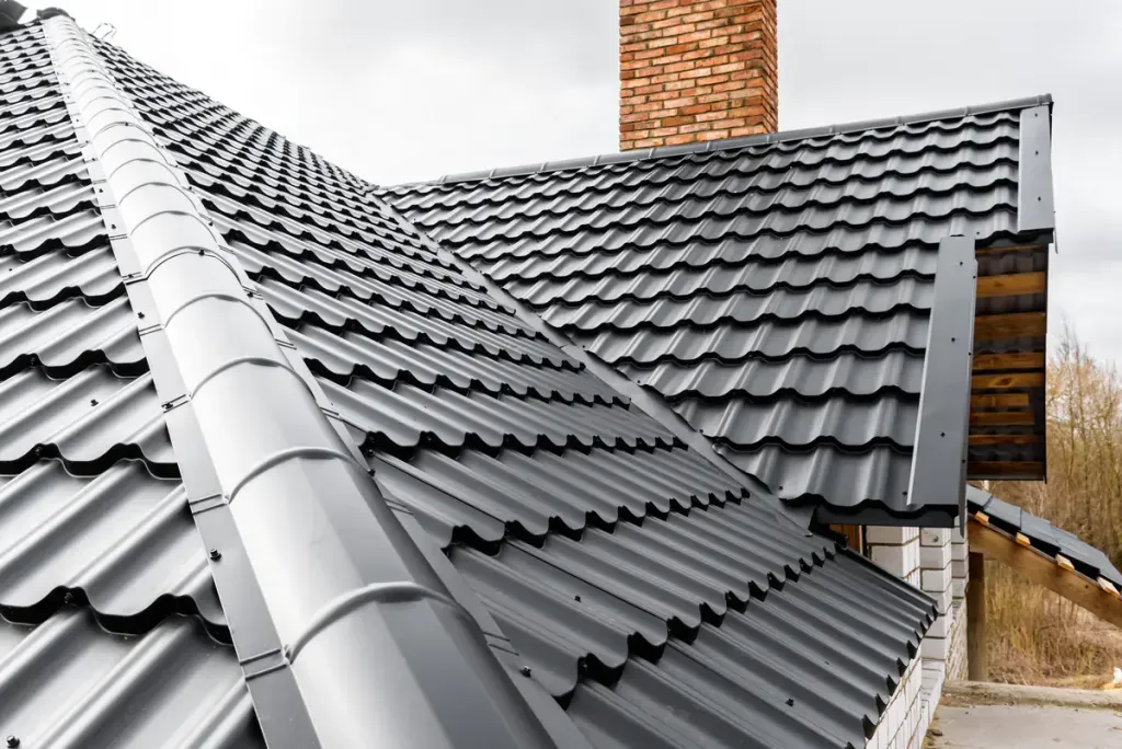 Pans de toiture en couverture métallique gris anthracite autour d’une cheminée en briques