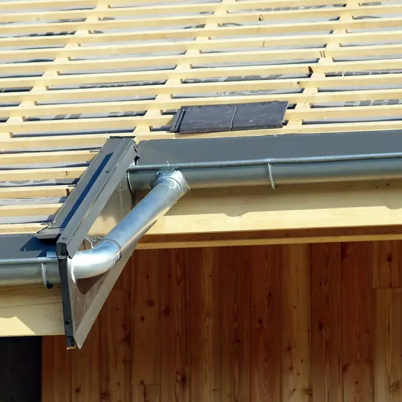 Raccord de gouttières métalliques et descente pluviale sur une toiture en cours de couverture