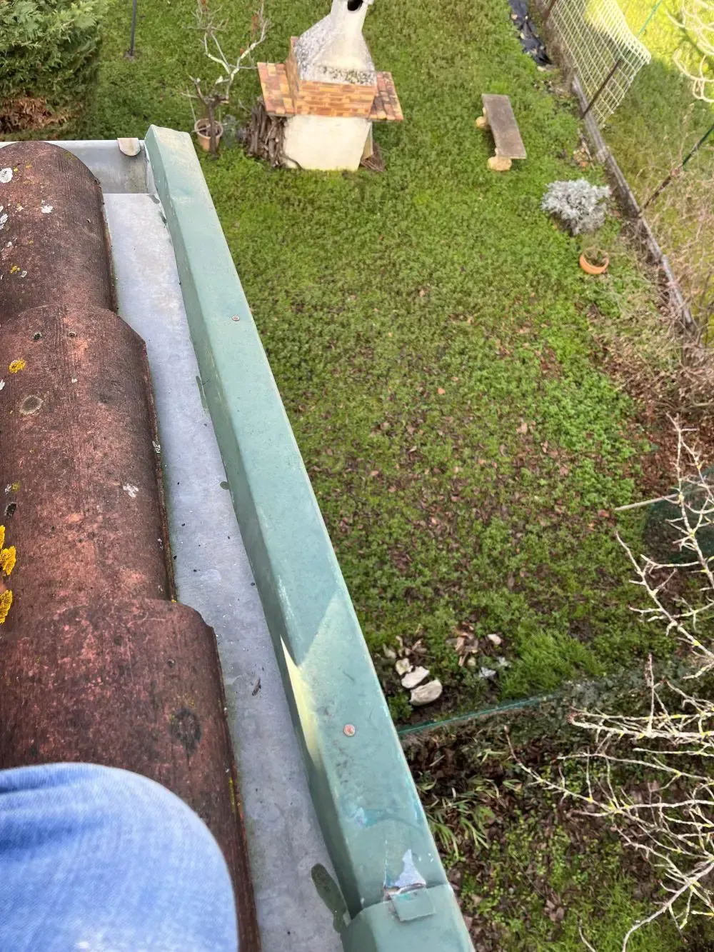 Gouttière en zinc le long d’une toiture en tuiles avec une bande de rive métallique verte
